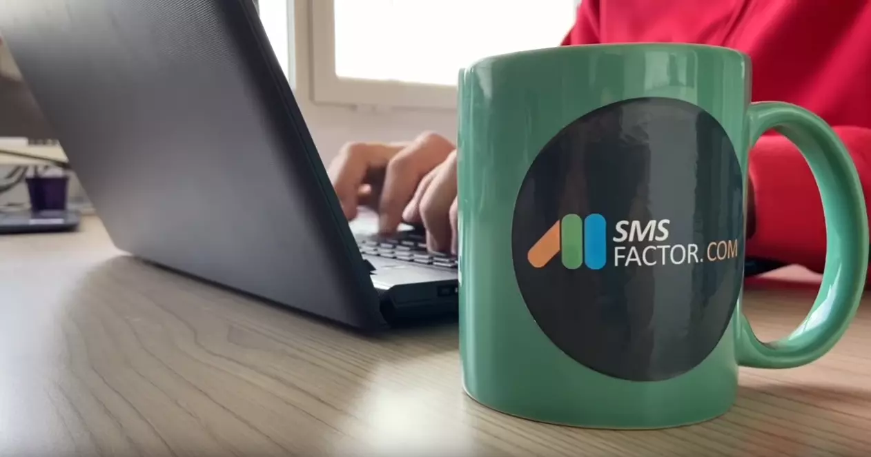 Tasse SMSFactor avec ordinateur en fond